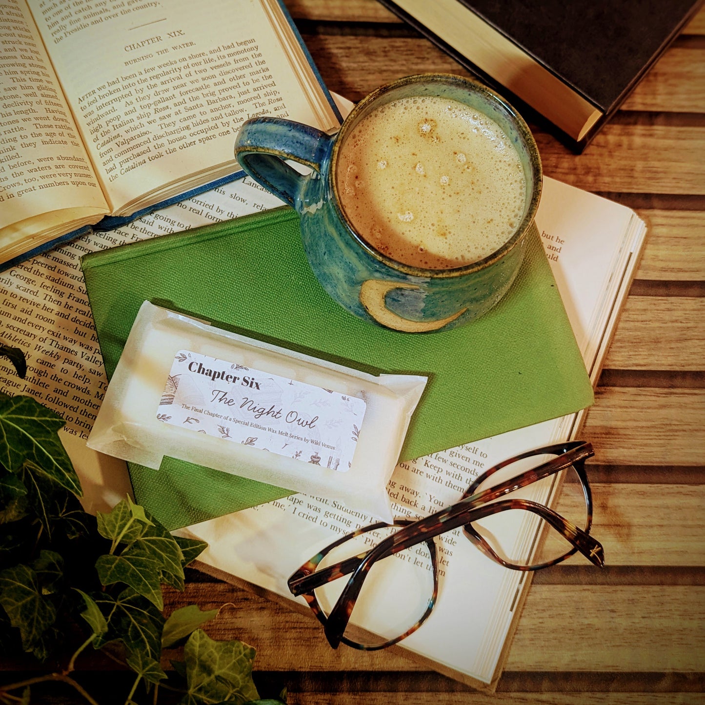Open book with a cup of coffee, glasses, and a wax melt on a wooden surface