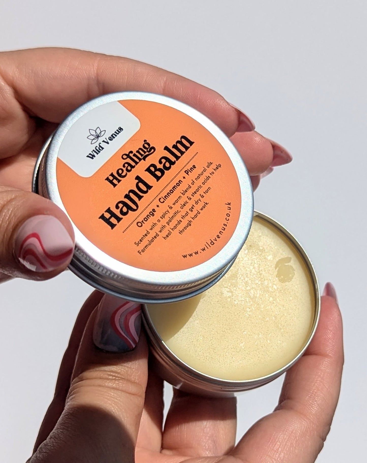 A pair of hands are shown holding the Healing hand Balm. The left hand holds the lid and shows the label, the right hand is holding the bottom half od the product which contains the hand balm.