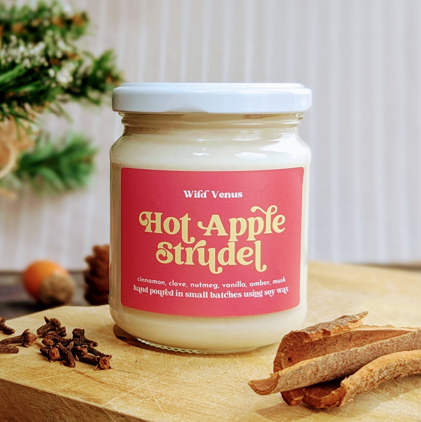 An apple and cinnamon candle is on a chopping board. Beside it are some sticks of cinnamon and cloves.