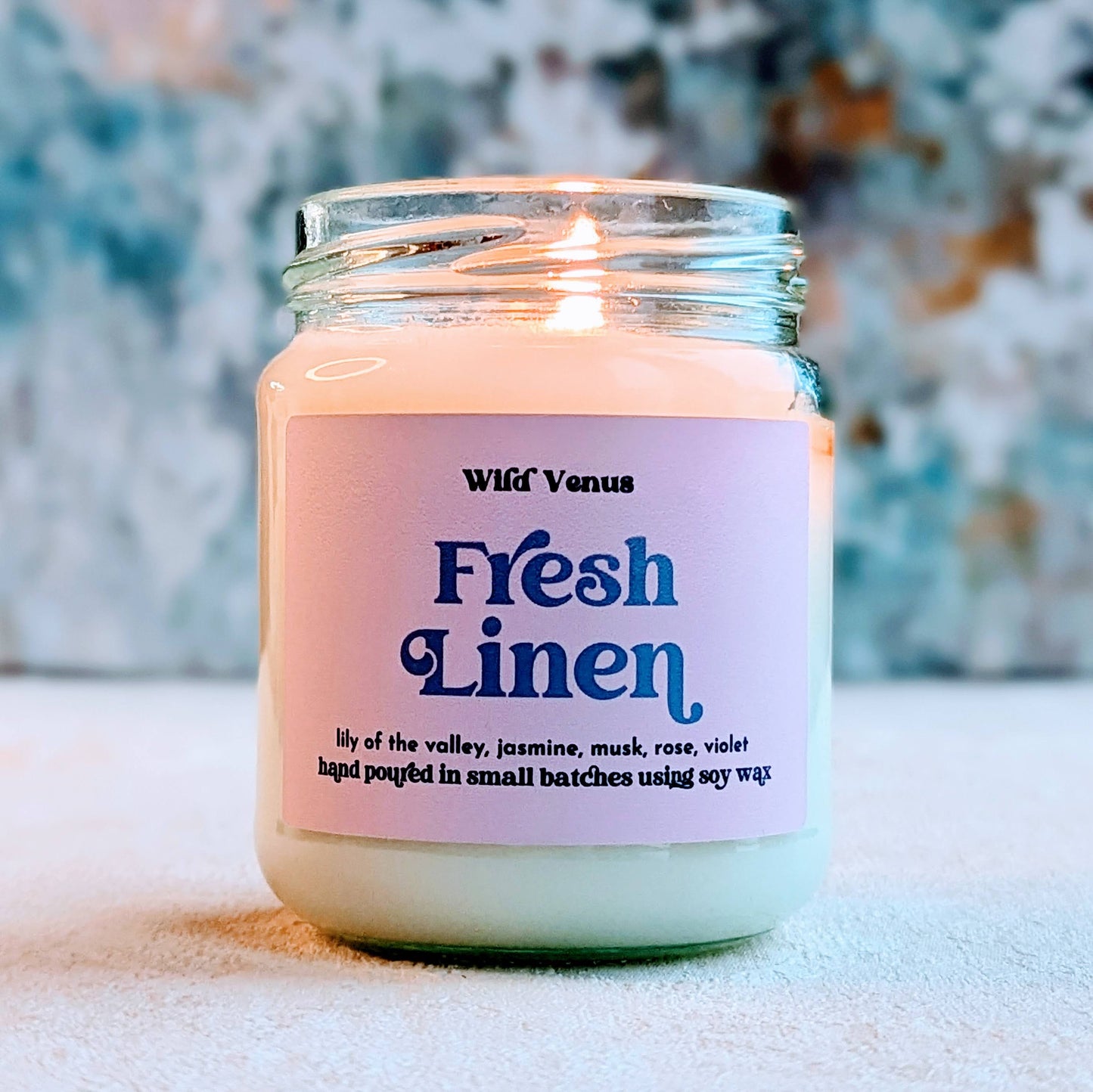 A lit fresh linen candle is glowing against a blue and textured background.