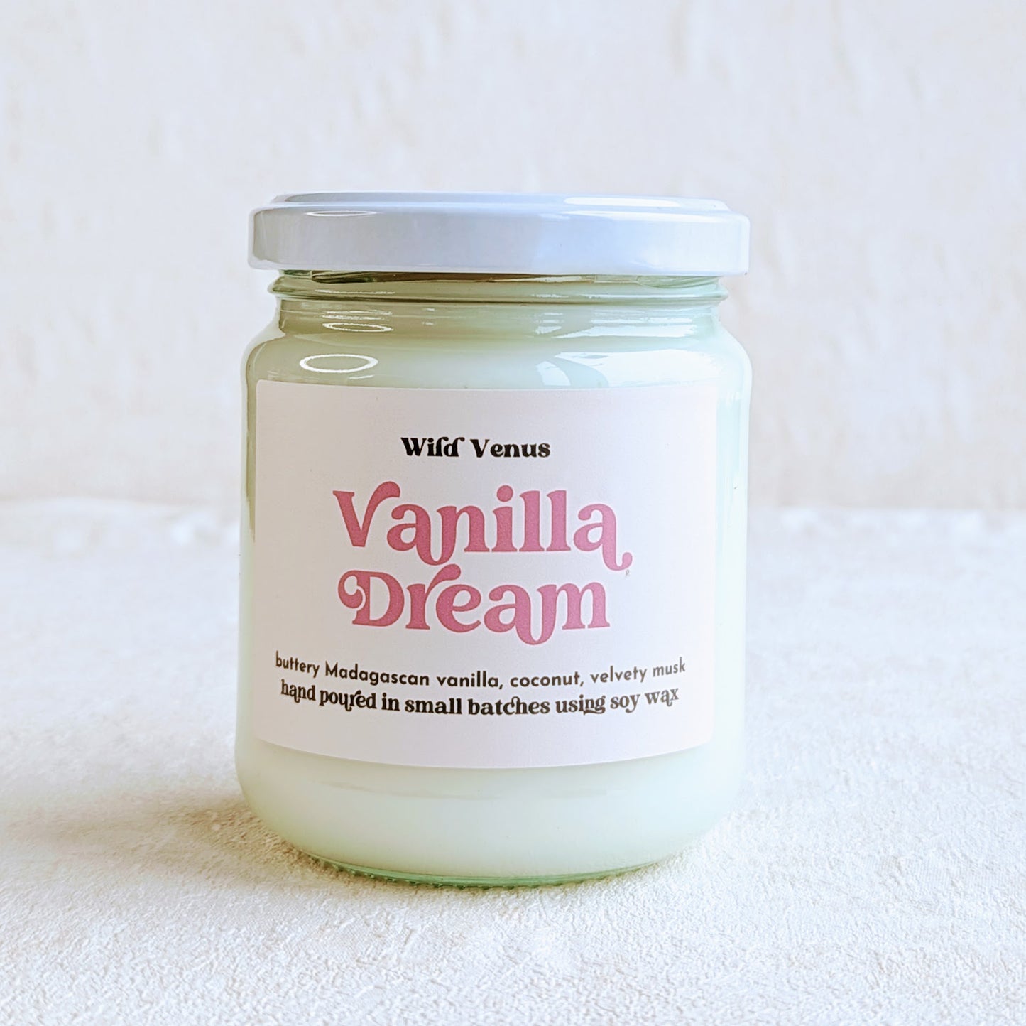 A soy candle with the label 'vanilla dream' in a retro font is shown against a plain white background and is cropped in a square frame.