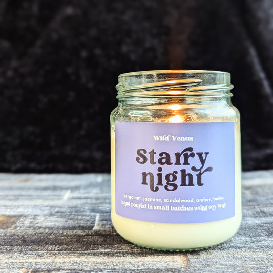 The starry night soy candle is lit and has been placed on a slate surface and is against a black background.