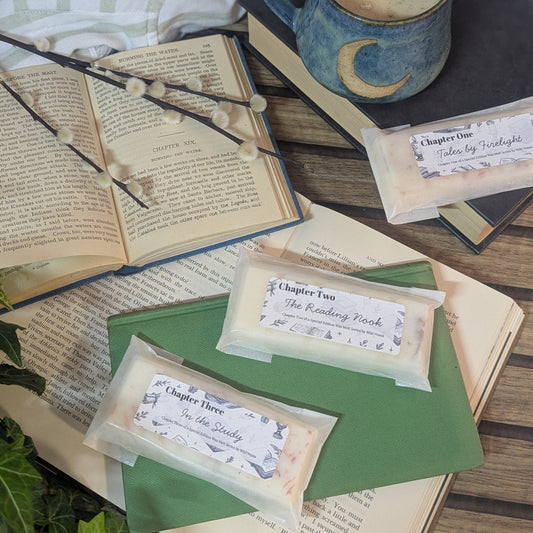 There are 3 wax melts which are on top of various books. There is a pretty mug beside them, some plants and a cotton striped shirt. 