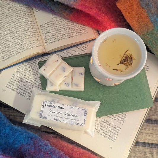 Open book with a cup of tea, wax melts, and a wax warmer surrounded by a colourful scarf background.