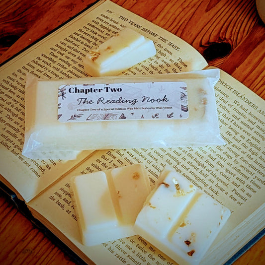 A wax melt is on top of an open book. Another wax melt has been broken into pieces.