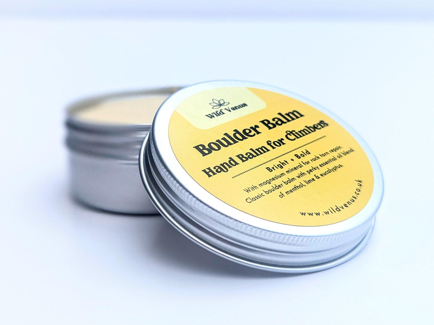 An open tin of Boulder Balm. The tin lid is resting on the edge of the open tin. The label is facing towards the camera.