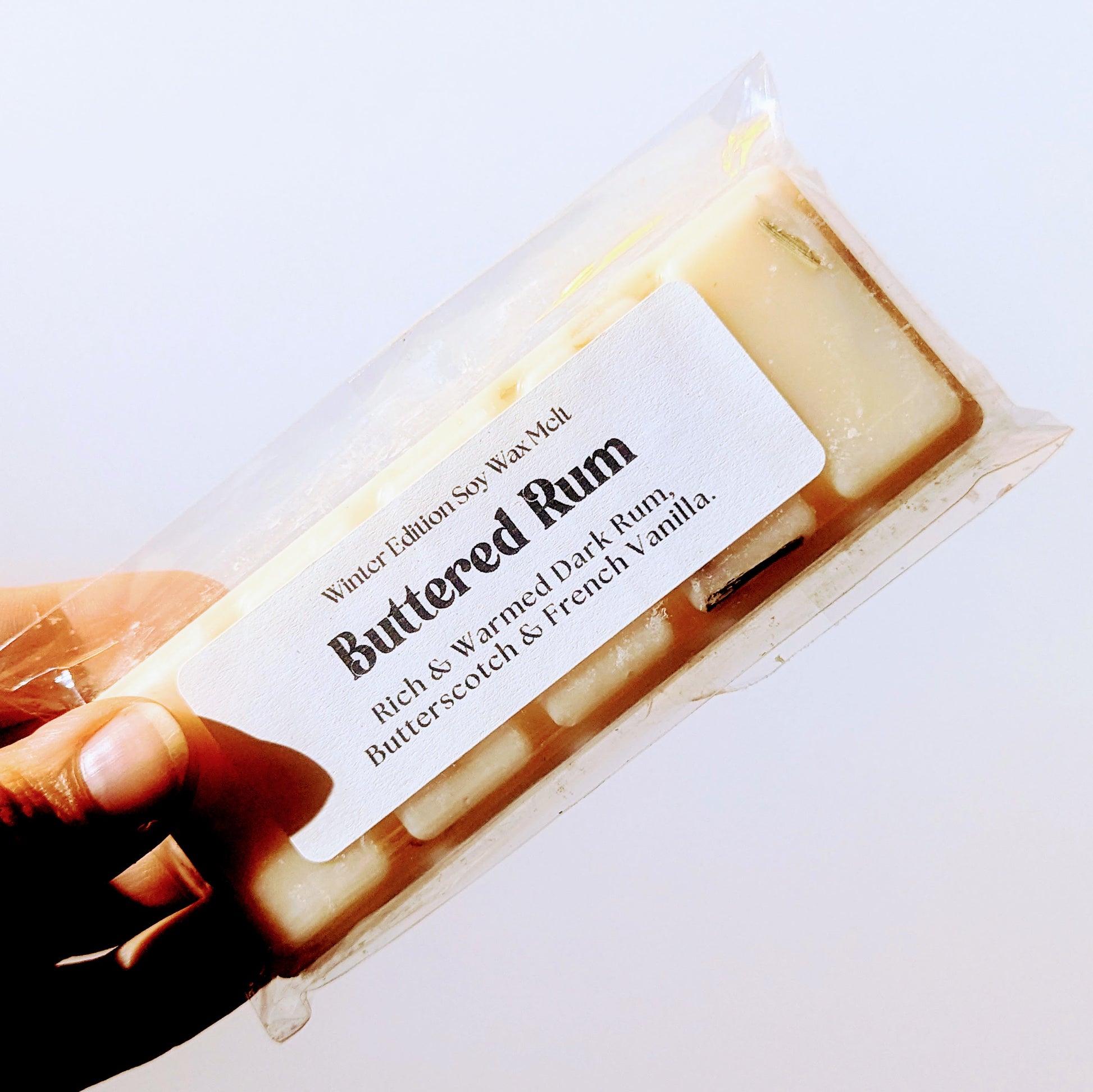 A hand holds the Buttered rum soy wax melt against a white background.