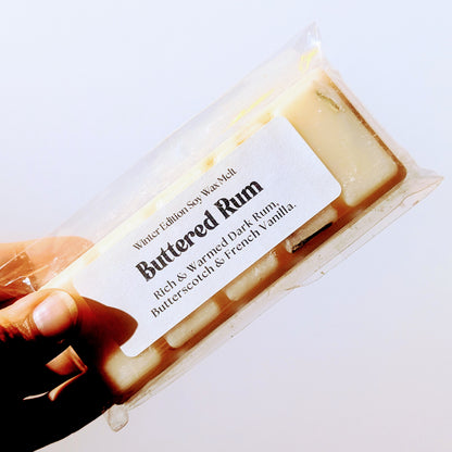 A hand holds the Buttered rum soy wax melt against a white background.