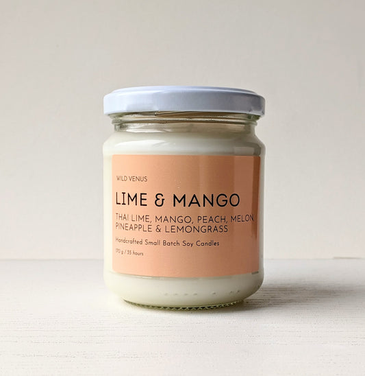 A lime and mango candle with a bright orange label against a white background.