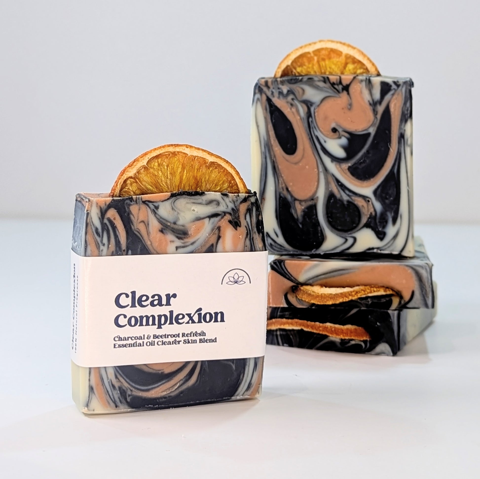 A soap bar with the words Clear Complexion on the label is infant of a small stack of other soaps.