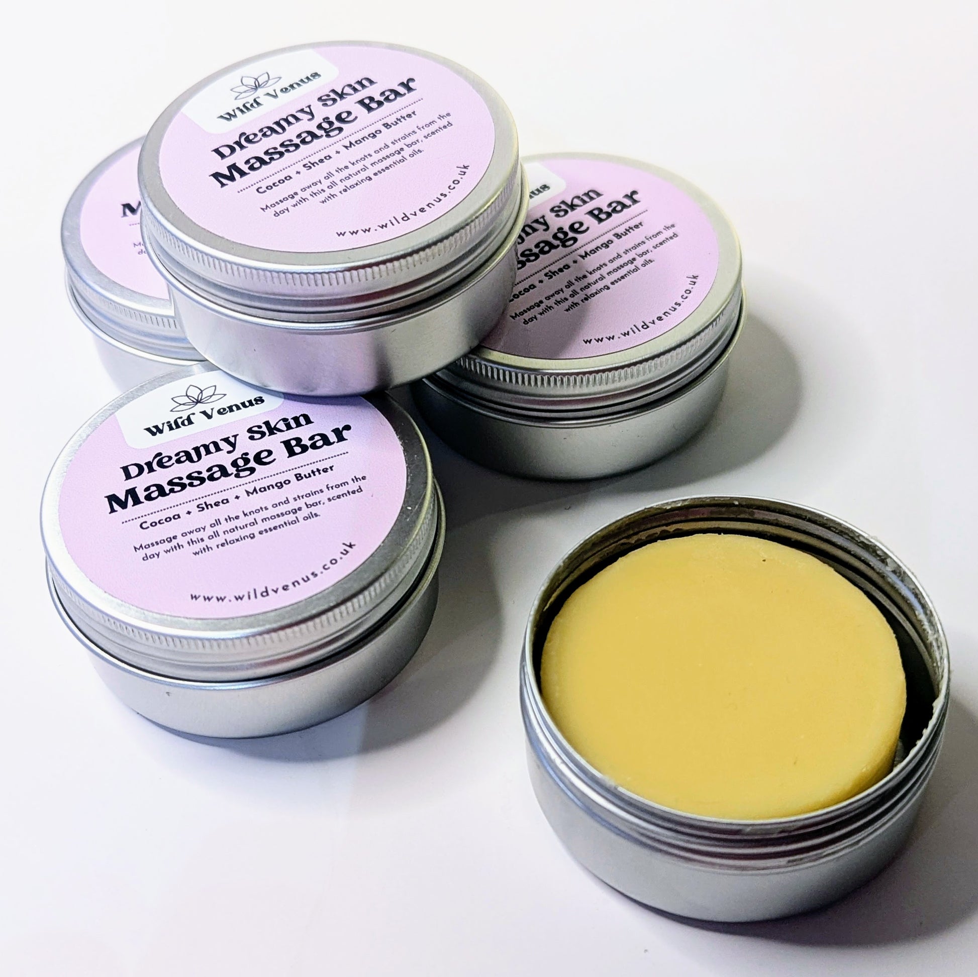 Four tins of the dreamy skin massage bars stacked and one open tin. 