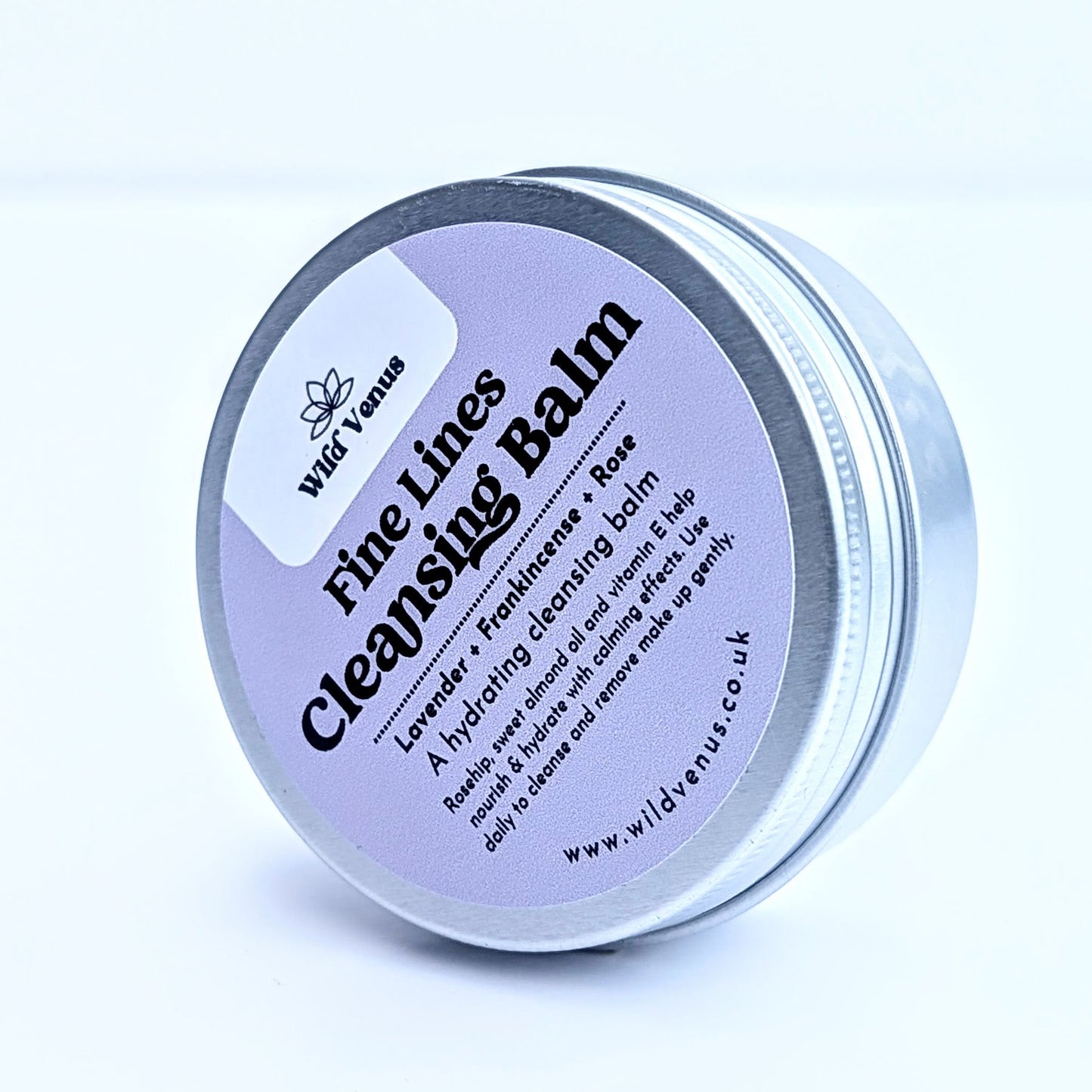 A tin of Fine Lines Cleansing Balm. This tin is on its side and tilted to the side on so you can see the whole label on the tin lid. The product is shot against a plain white background. 