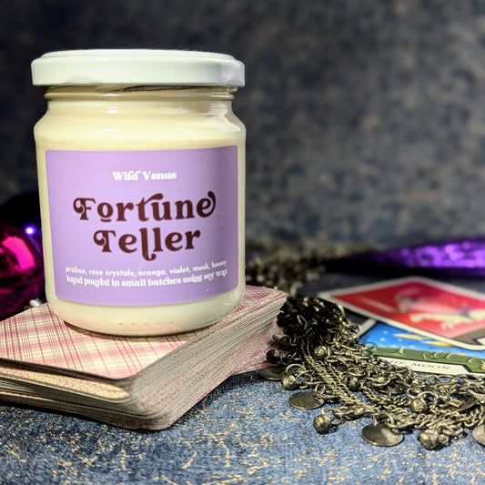 Fortune teller candle on top of tarot cards and some gypsy silver next to it. The background in a deep blue veined with gold. 