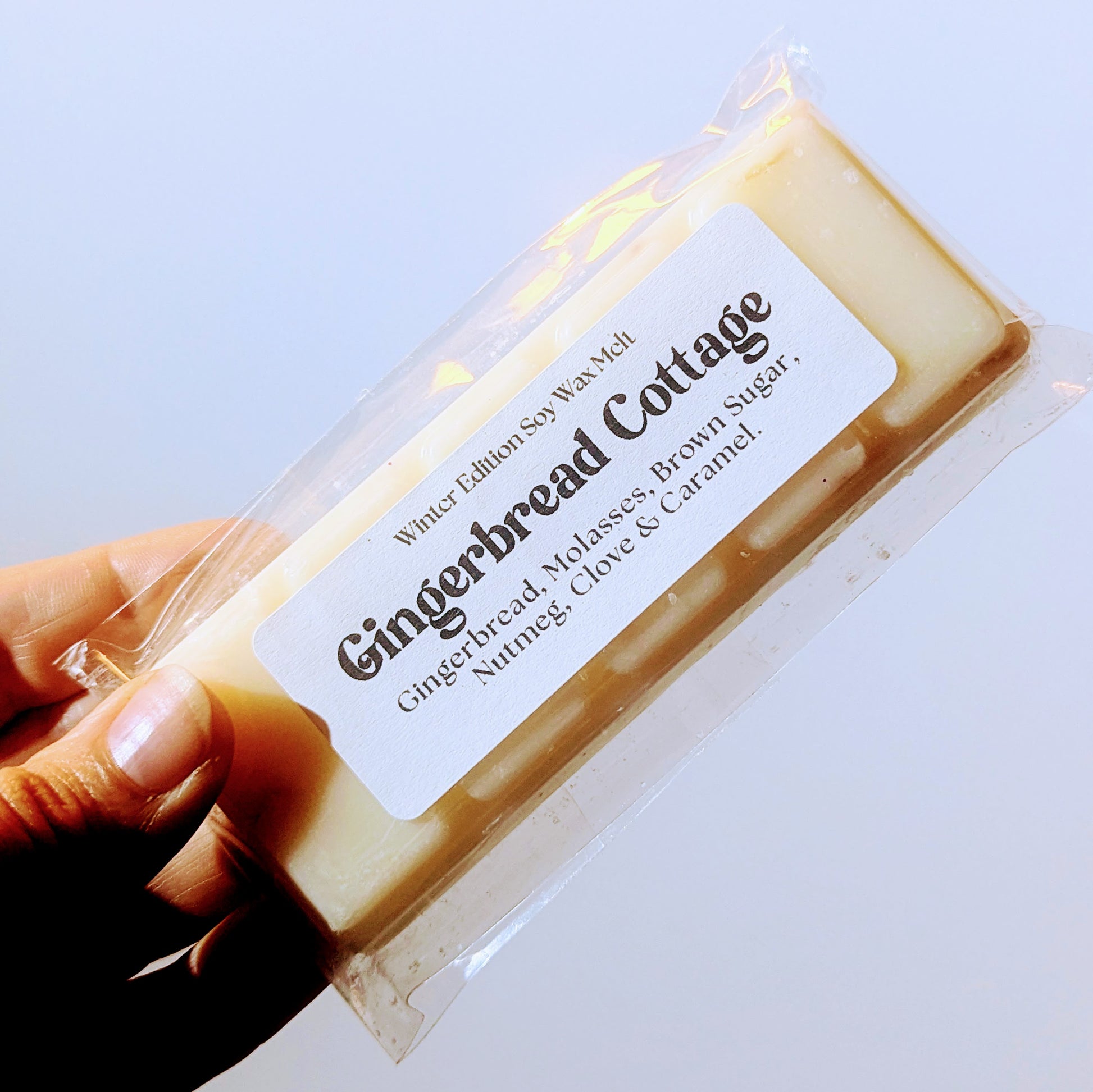 A hand holds the gingerbread cottage soy wax melt against a white background.