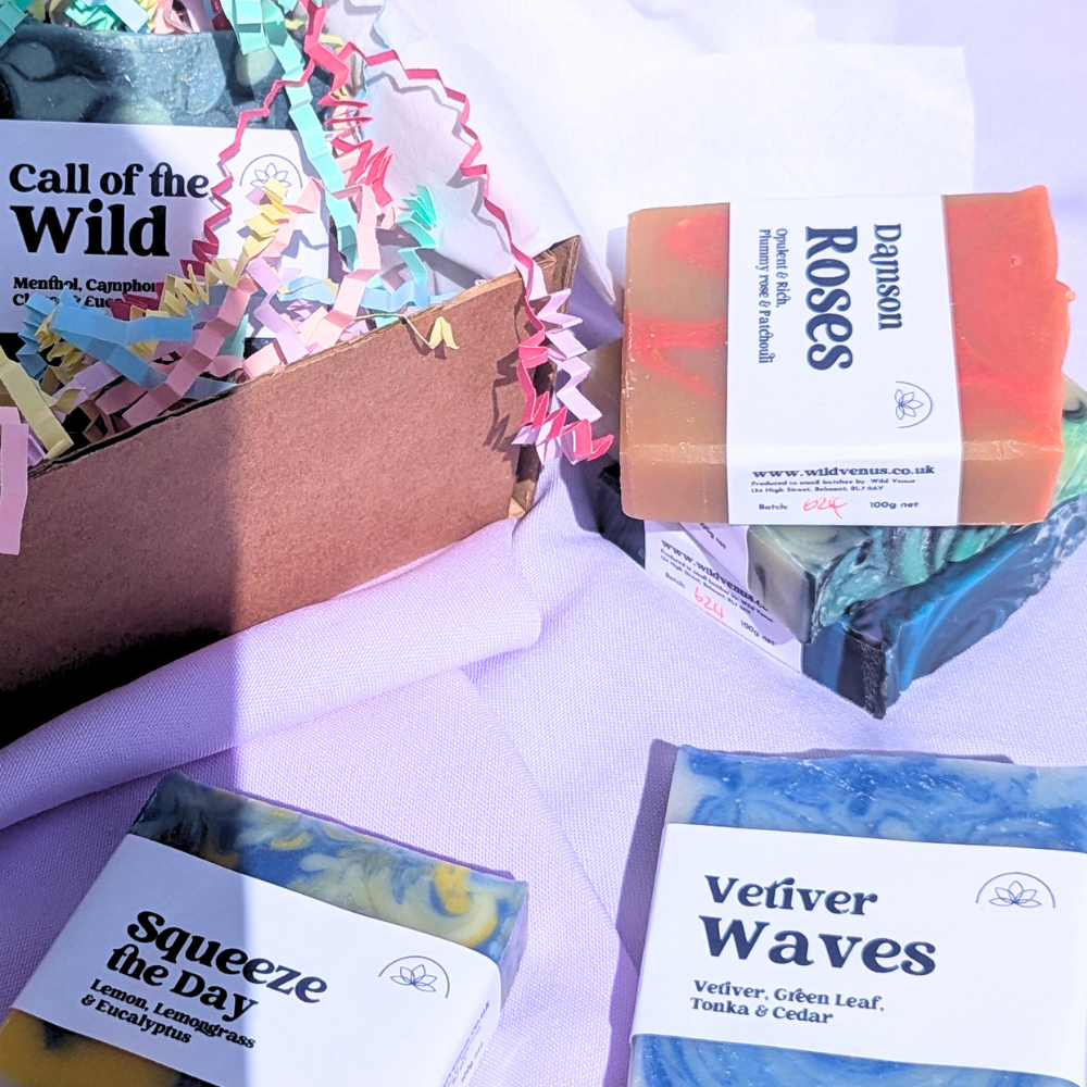 Photo shows 5 soap bars in and around an open box with a shadow cast across the soaps. 