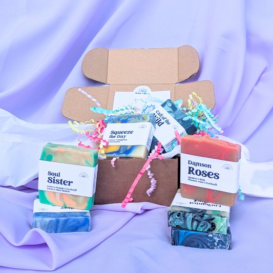 Photo shows 5 soap bars in and around an open box against a lilac background. 