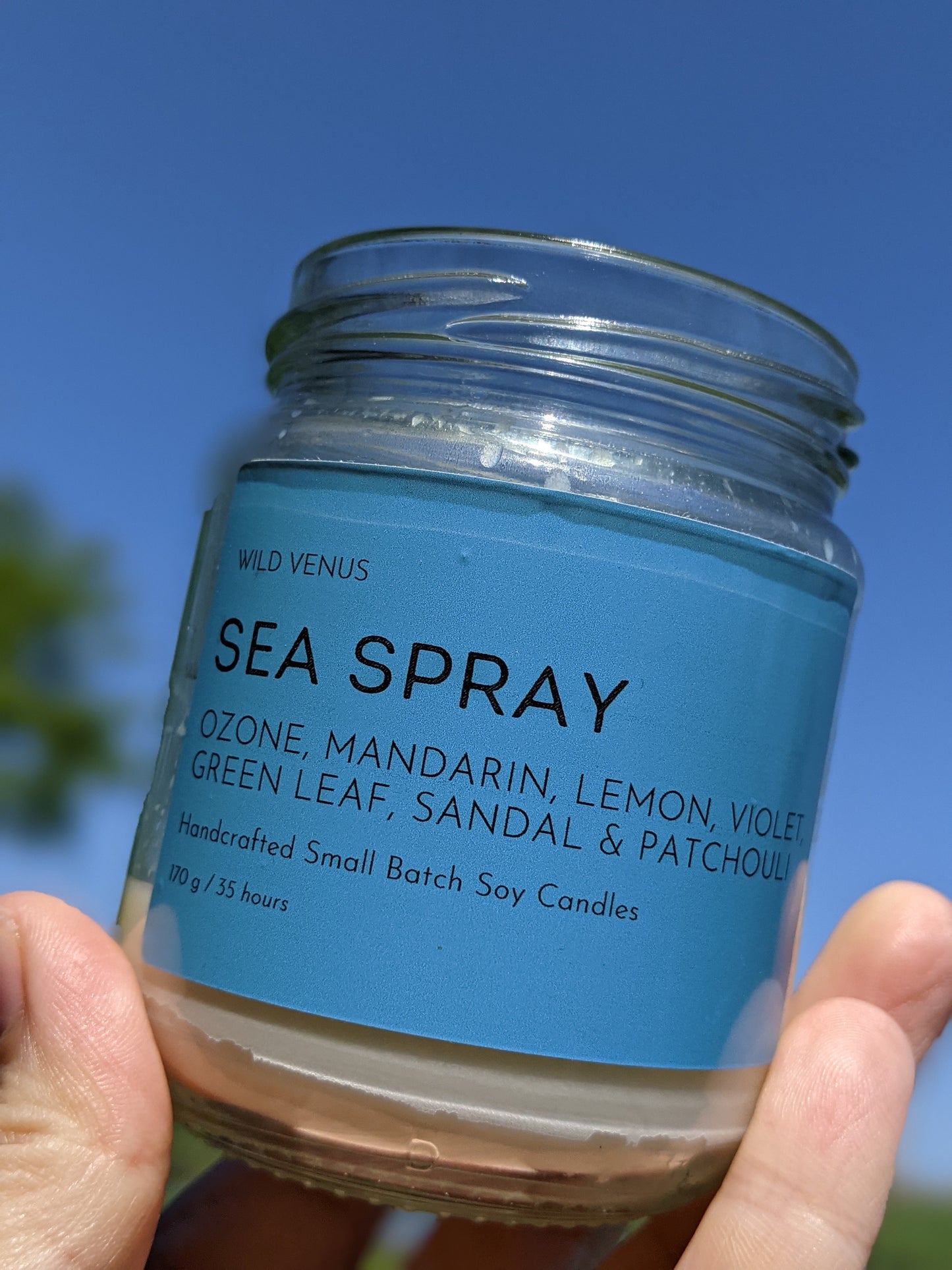 A used Sea Spray scented candles held up against a very blue sky.