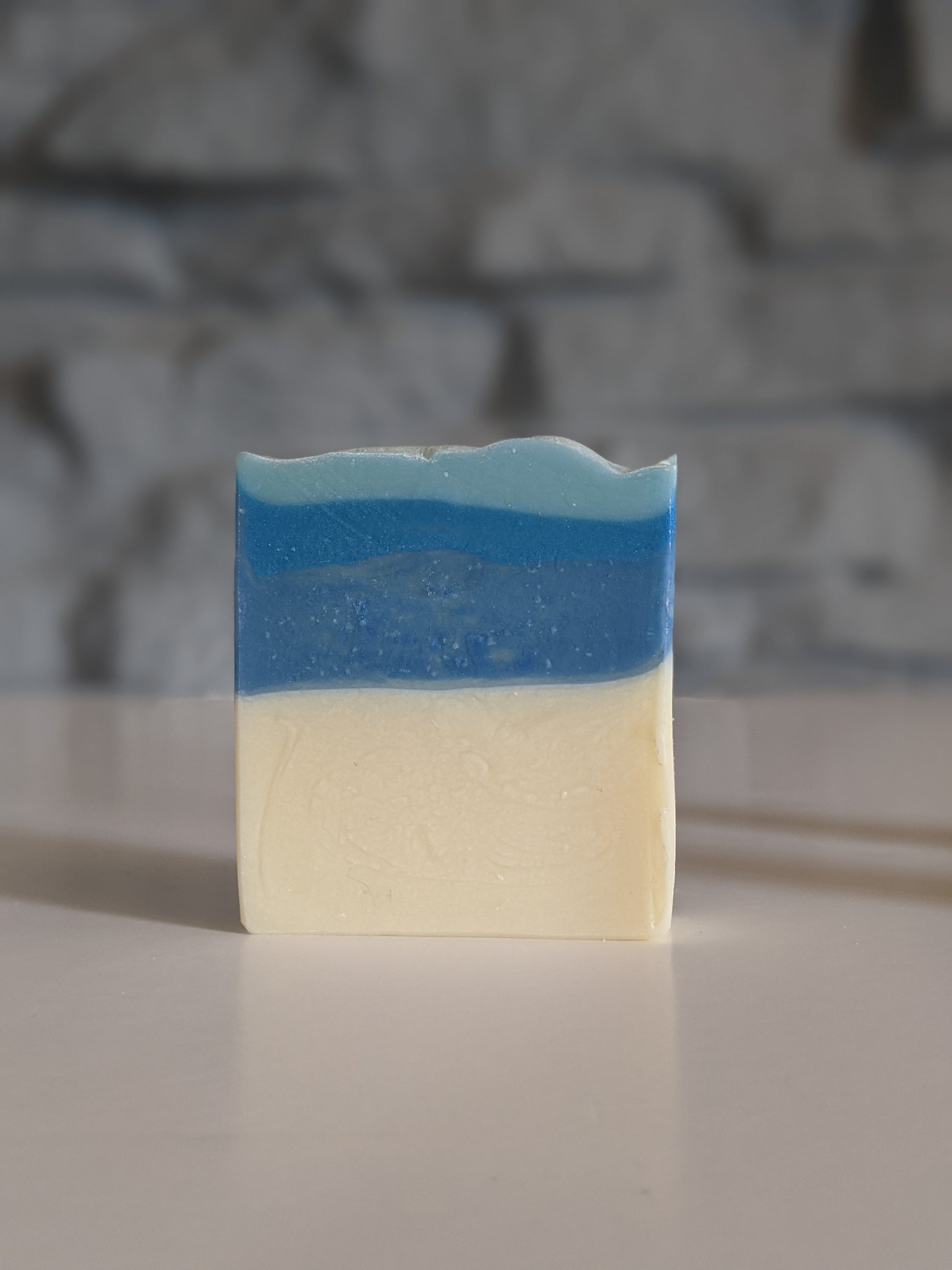 A bar of the Ice queen vegan soap bar on a white surface against aa light grey brick background. 