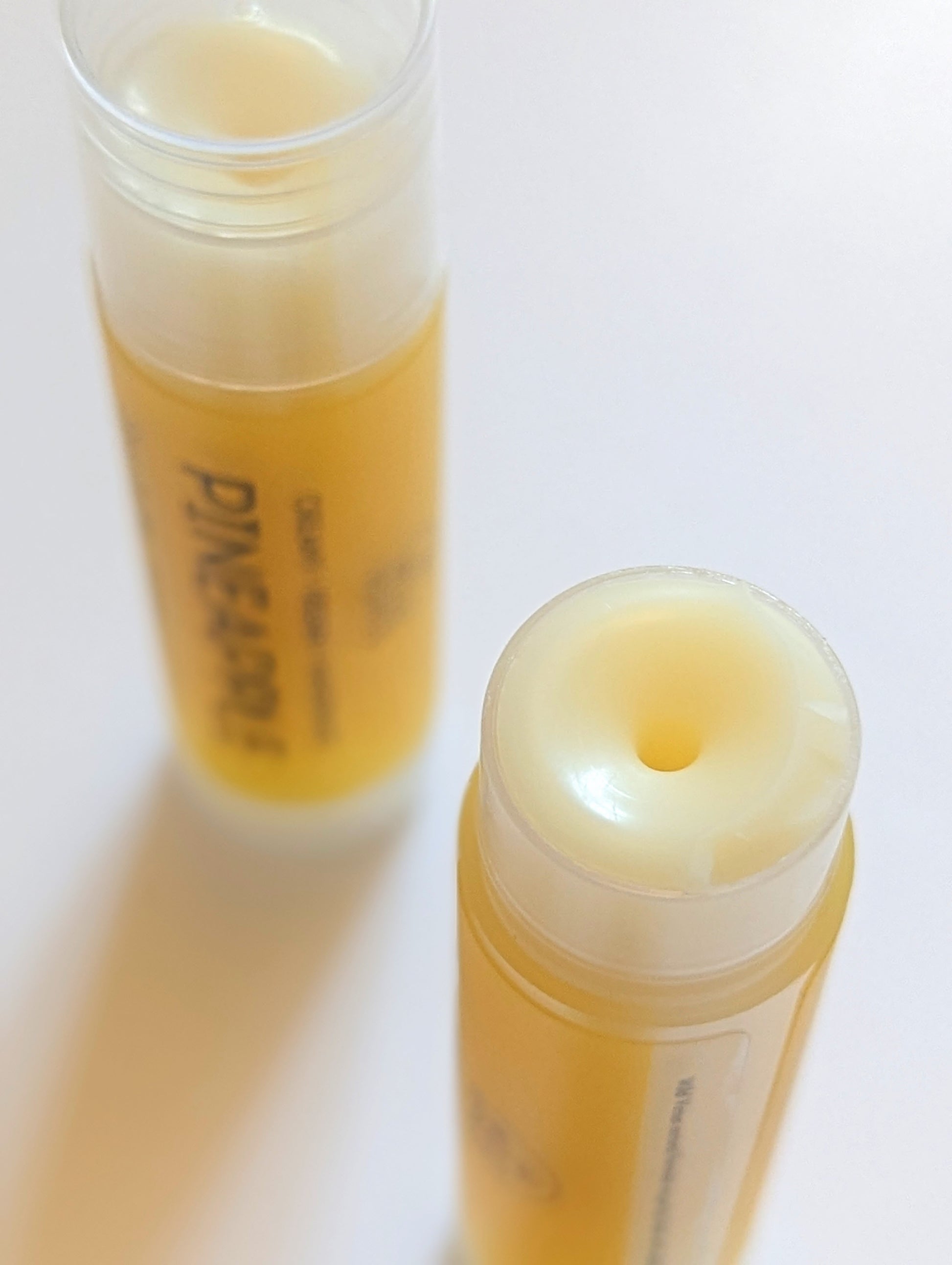 Two tubes of Pineapple Lip Balm with the top off close up.