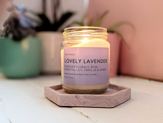 A lit Lovely Lavender candle on a pink coaster. 
