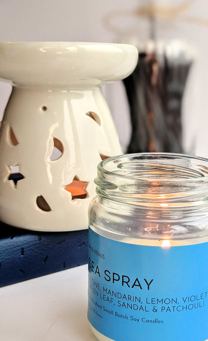 A sea spray scented soy candle is burning in front of a white oil burner. Some matches are in the background. 