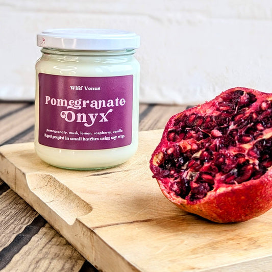A pomegranate soy candle is on a wooden chopping board with a halved pomegranate fruit beside it.