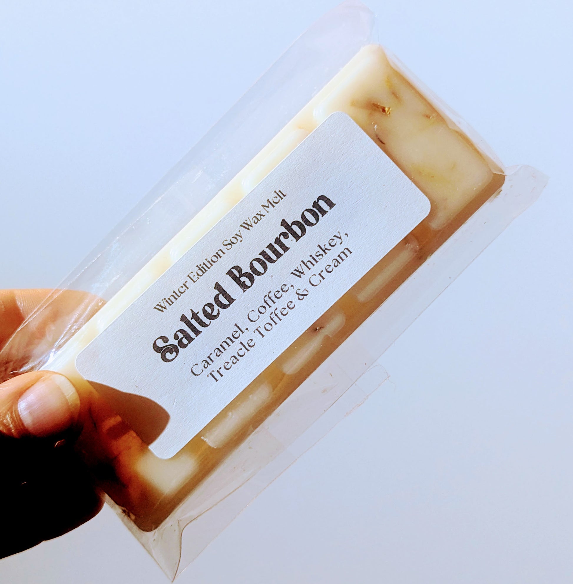 A hand holds the salted bourbon soy wax melt against a white background.