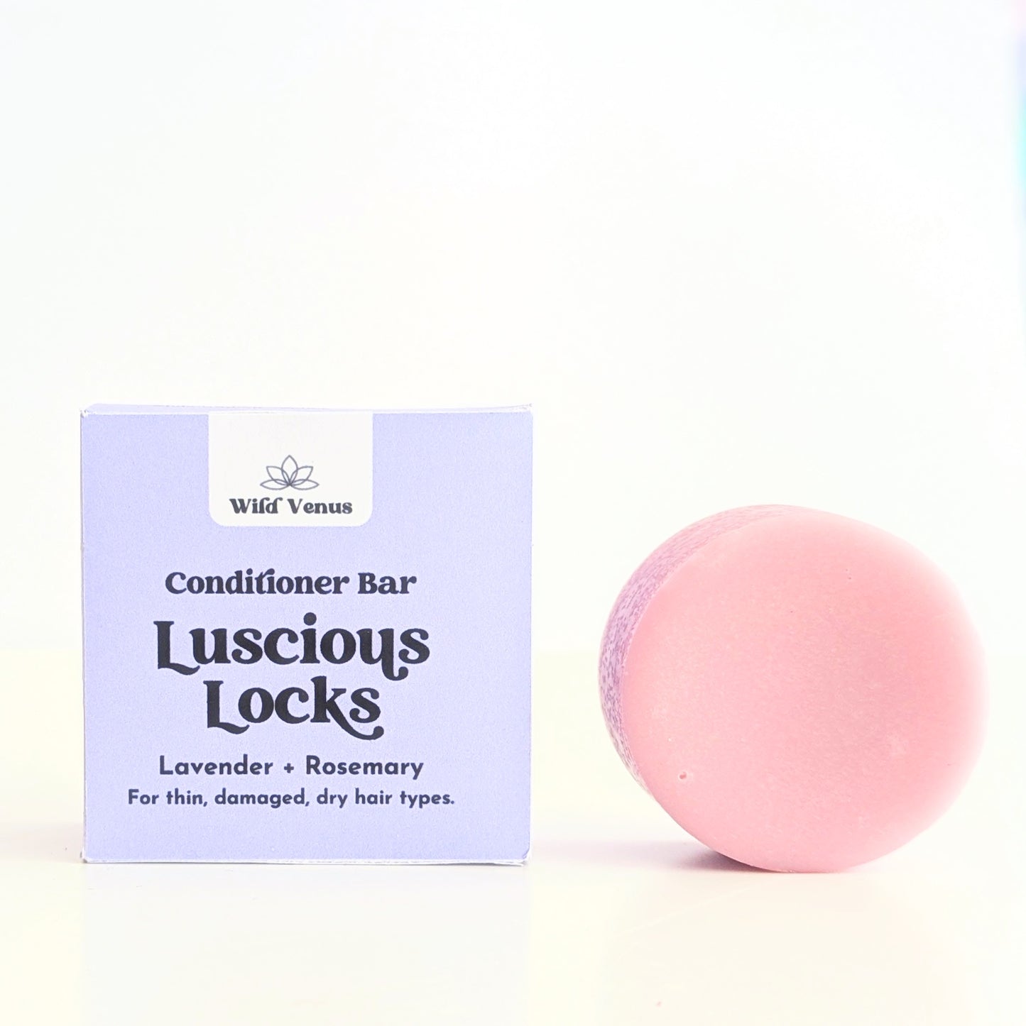 A Luscious Locks lavender hair conditioner bar is to the right of a box. The conditioner bar and packaging is against a white background.
