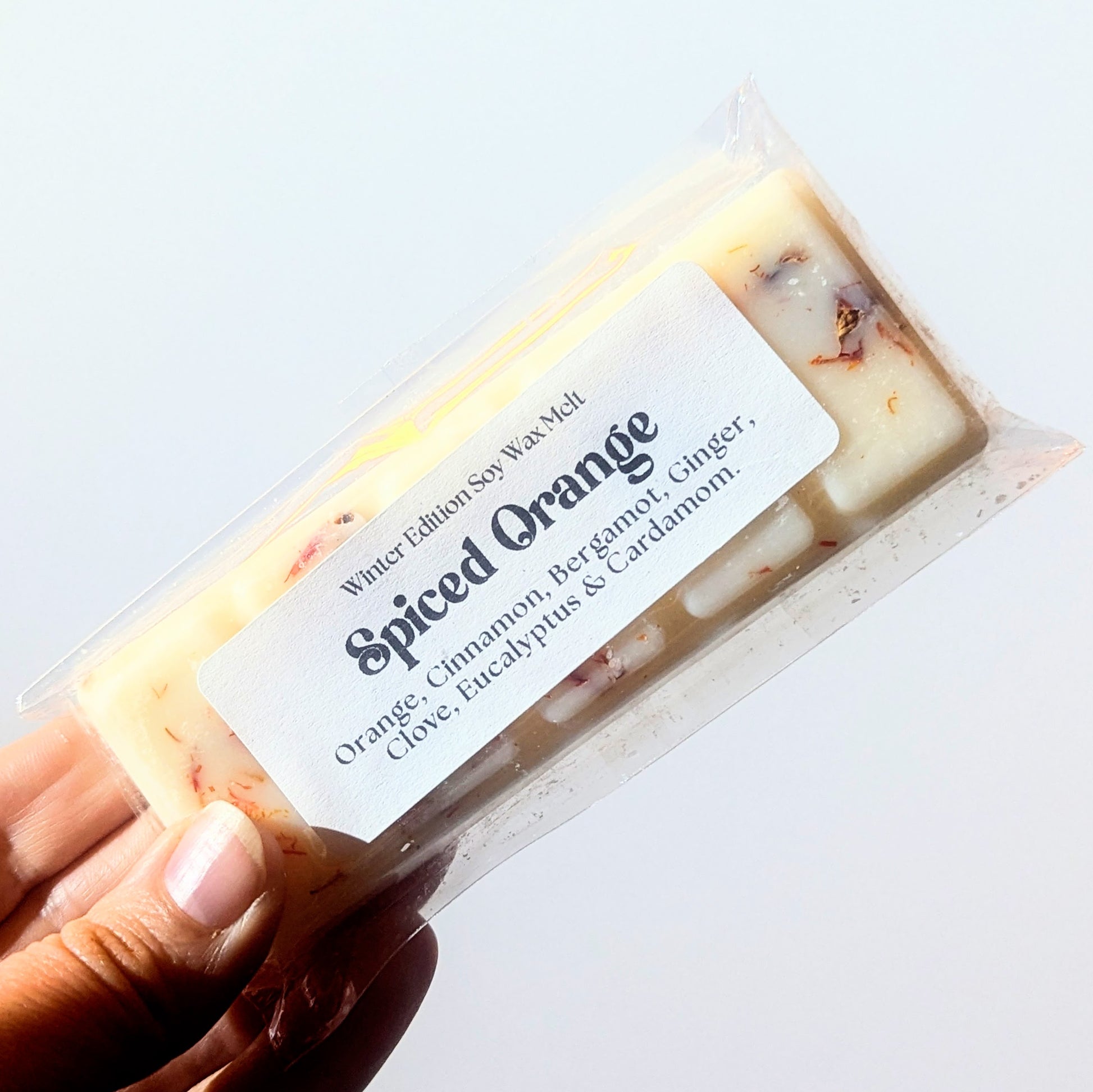 A hand holds the spiced orange soy wax melt against a white background.