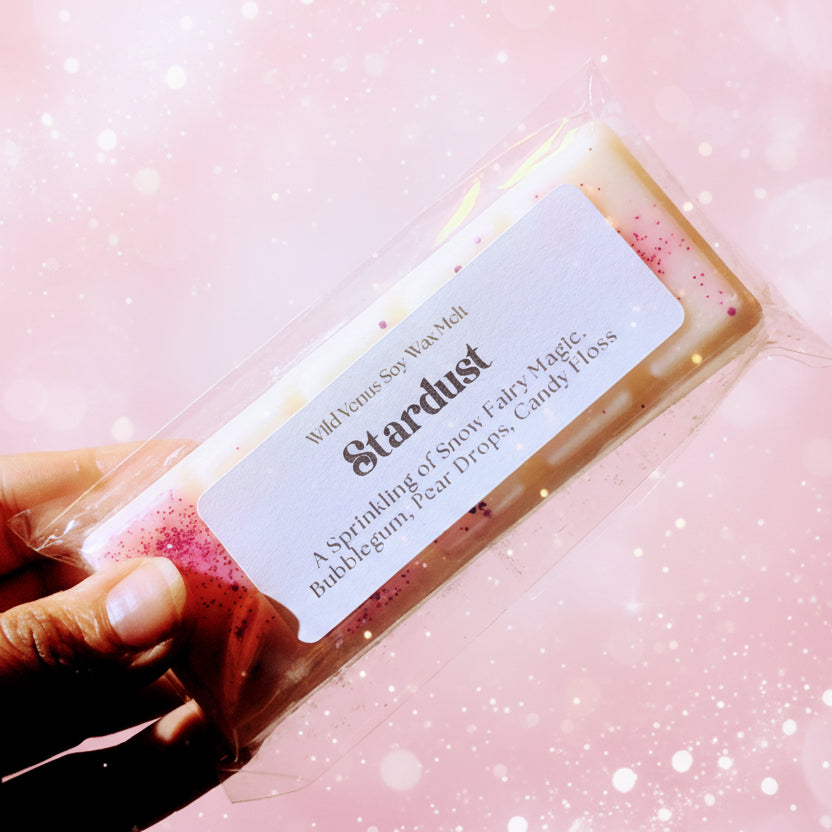 Holding the stardust soy wax melt against a sparkly pink background.