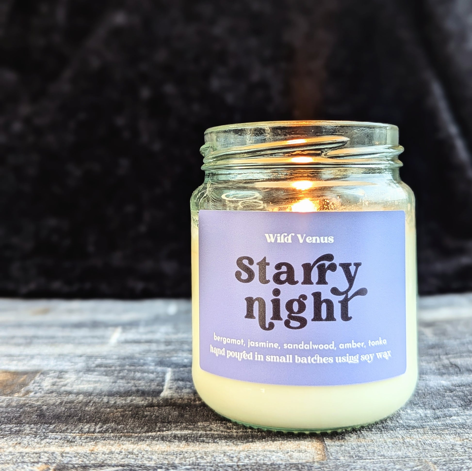 The starry night soy candle is lit and has been placed on a slate surface and is against a black background.
