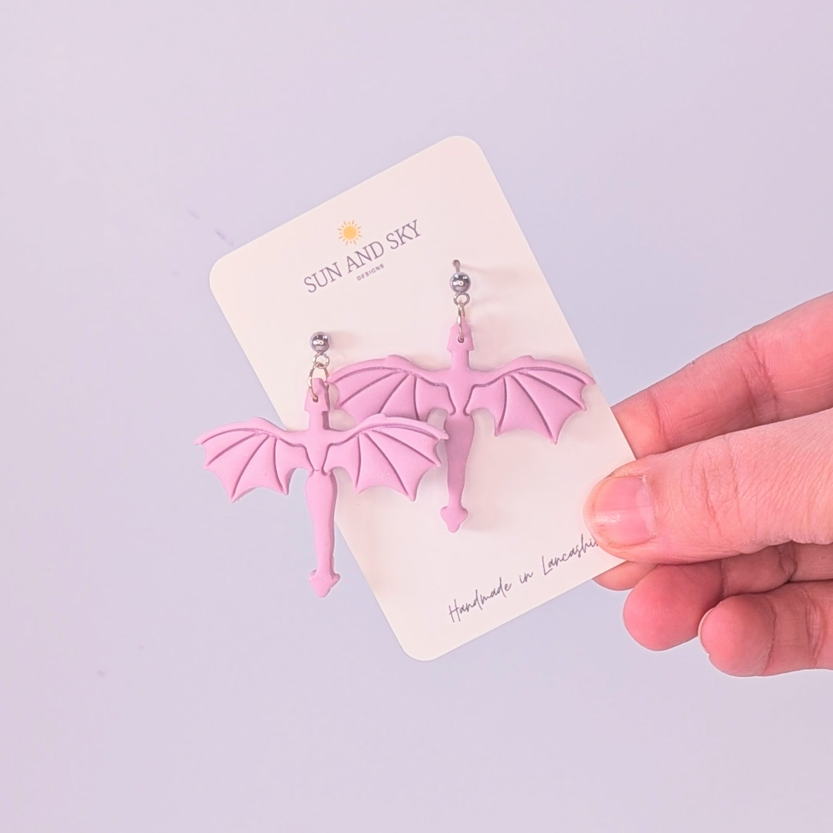 Holding lilac dragon earrings by sun and sky designs. 
