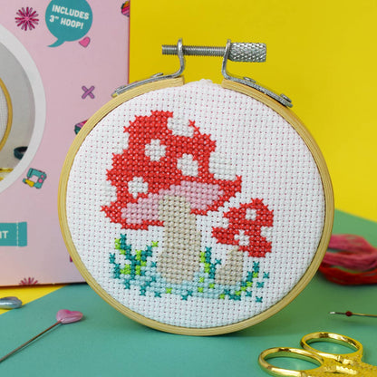 A close up photo of the completed 'Toadstool' mini cross stitch kit next to the presentation box.