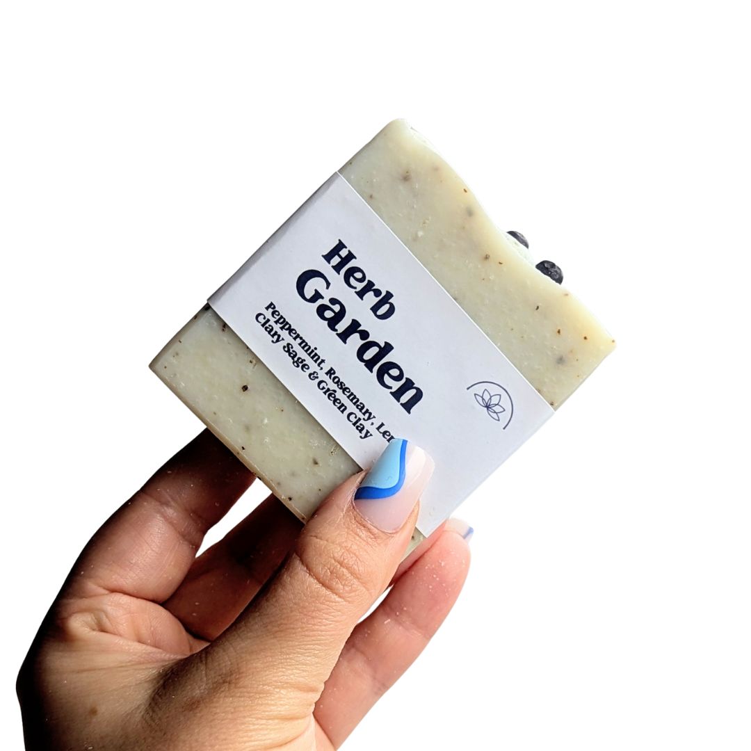 A hand holds a herb garden soap against a white background. 