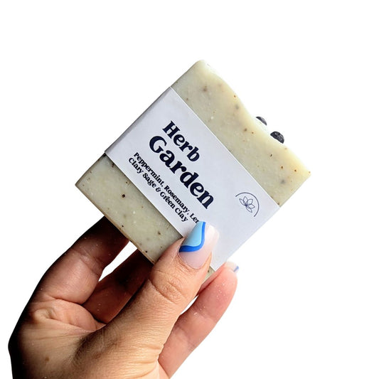 A hand holds a herb garden soap against a white background. 
