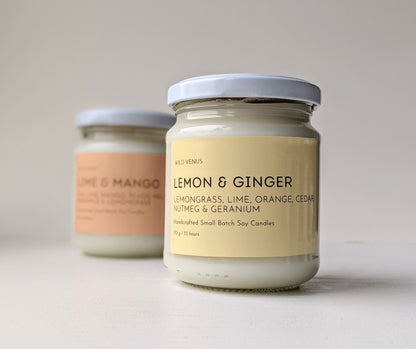 A lemon and ginger soy candle is in front of a lime and mango candle. Both candles are in front of a plain white background. r 
