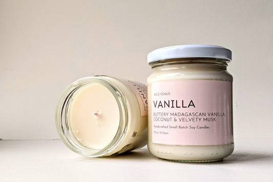 A Vanilla scented candle and another vanilla candle on its side against a white background. 