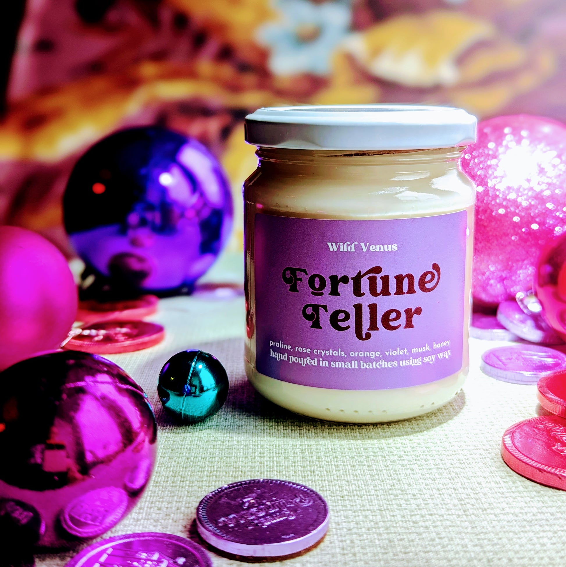 fortune teller soy wax candle is surrounded by shiny baubles, pink and purple coins. 