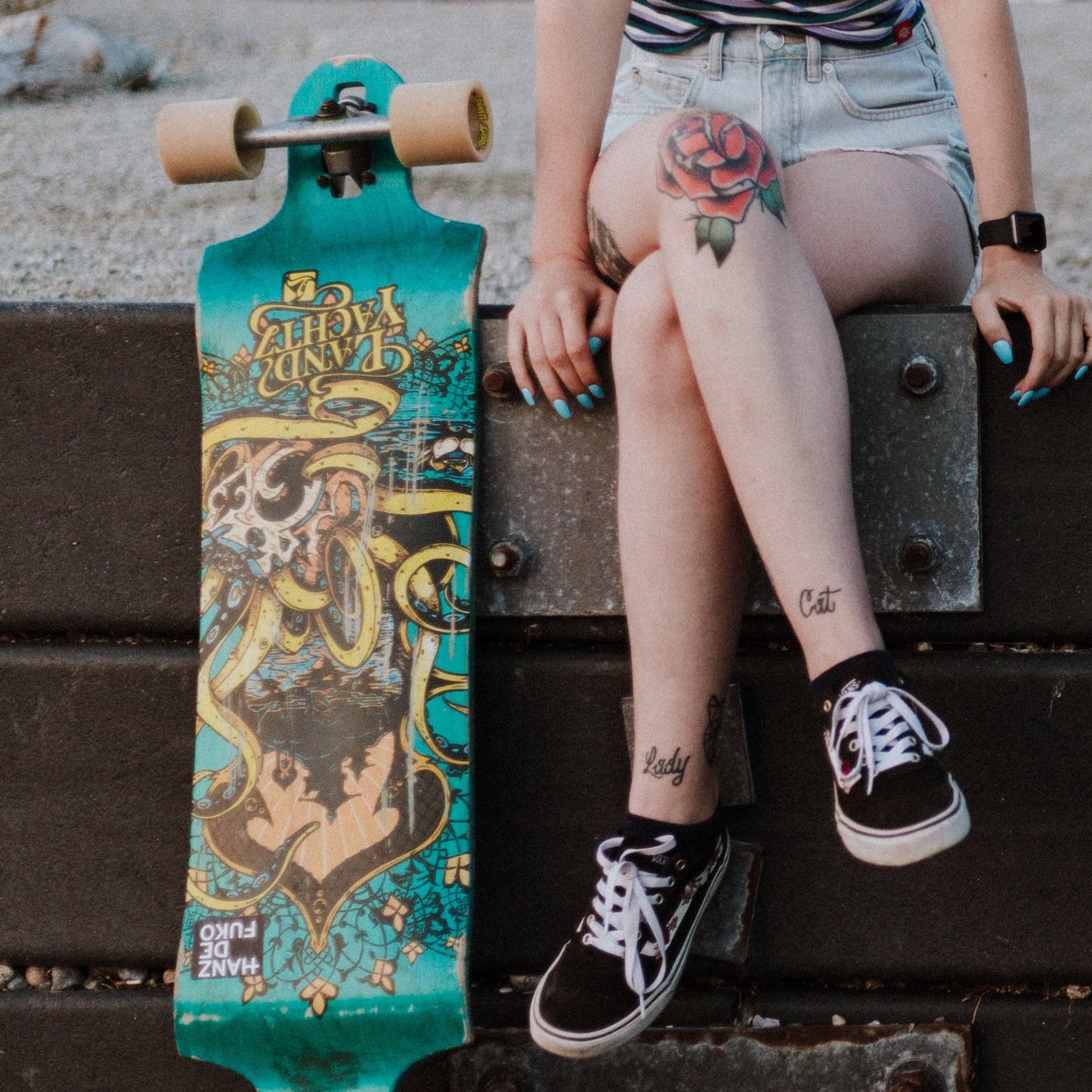 Photo of tattooed girl sitting outside with a skateboard beside her. Photo by Priscilla du Preez  
