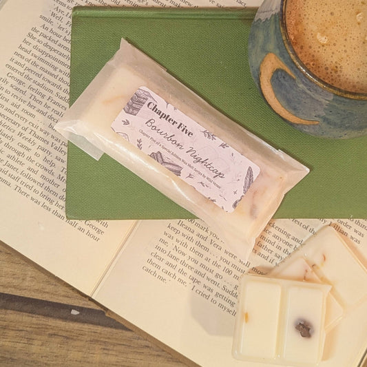 wax melts with a label on top of an open book next to a cup of coffee.