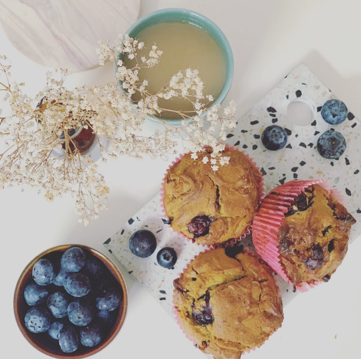 Blueberry and vanilla muffins on a table with a sprig of a white flower.