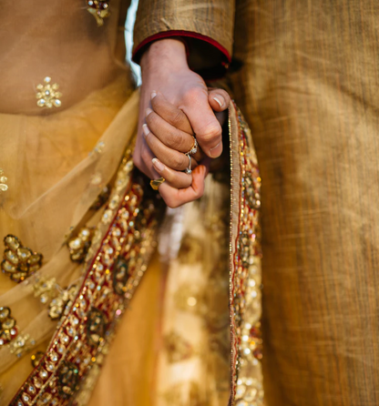Two people wearing Indian dress hold hands. 