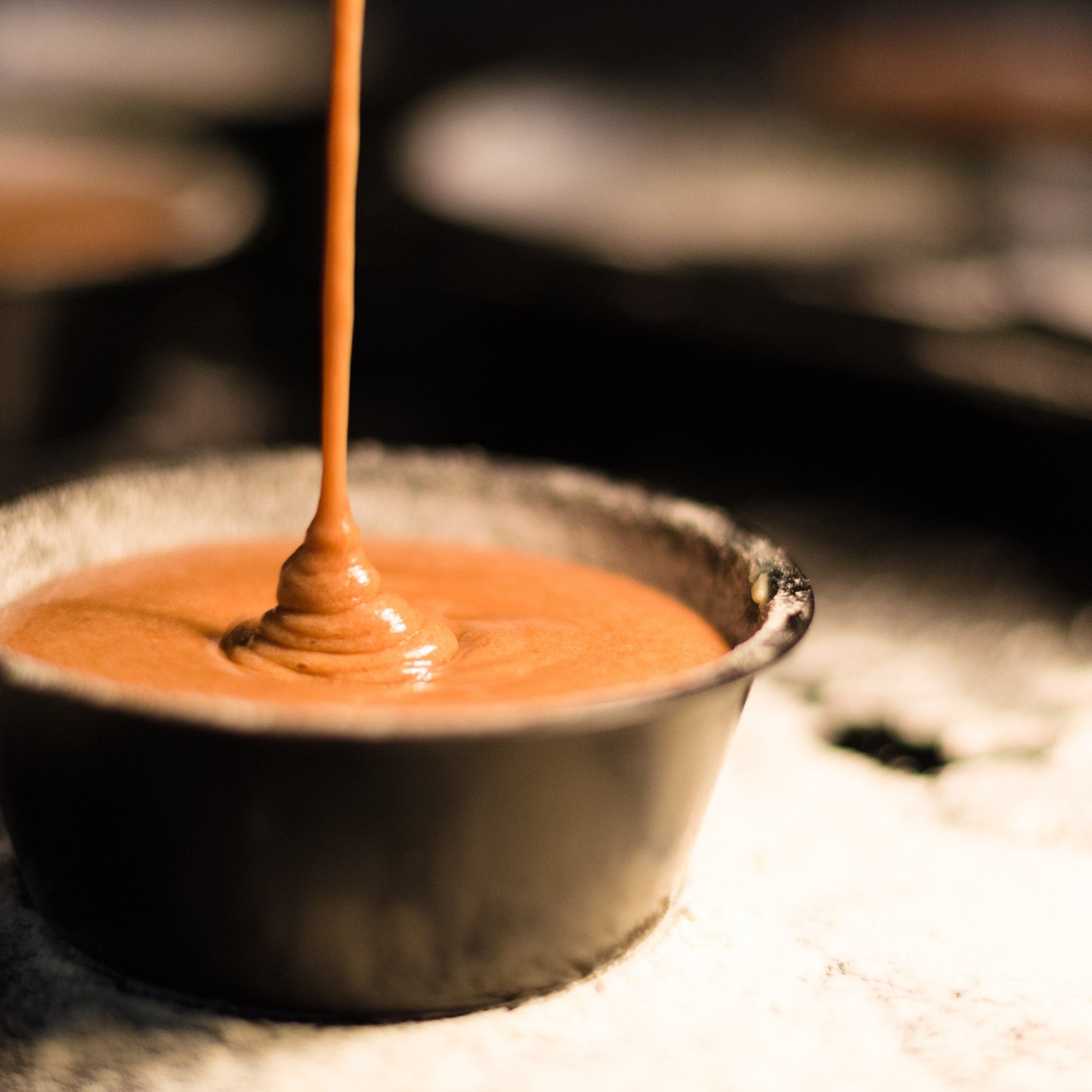 A ceramic pot almost full to the brim of delicious caramel being drizzled in.